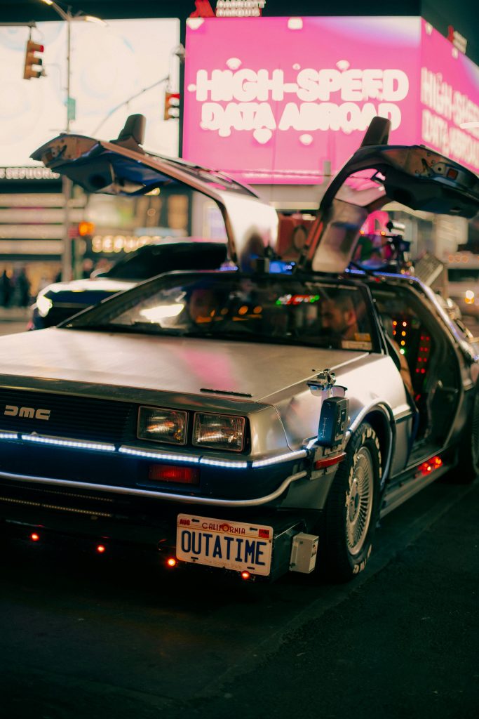 Delorean car with doors that rise up. Car parked on a city street with a pink digital billboard in the background