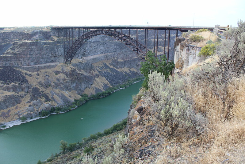 arched bridge that spans over a tall canyon with a green river below.