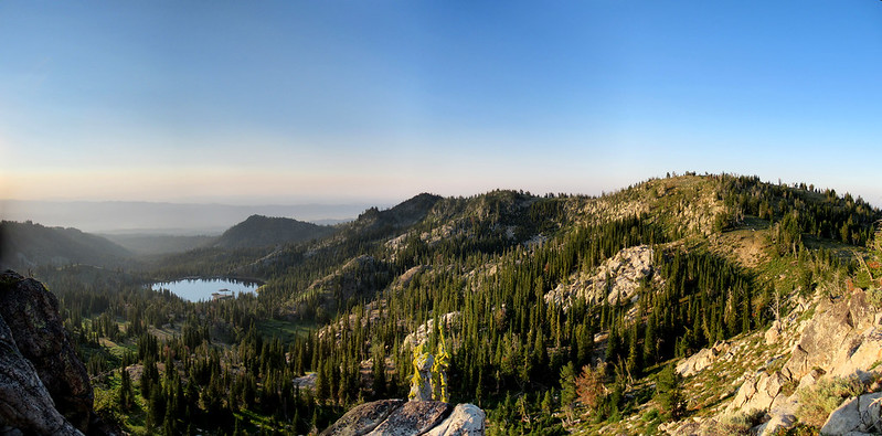 top of mountain view with rocks and trees in the foreground and a lake in the background