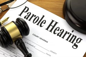 A picture of a court hearing form with parole hearing written at the top together with a gavel, block, pen and glasses.