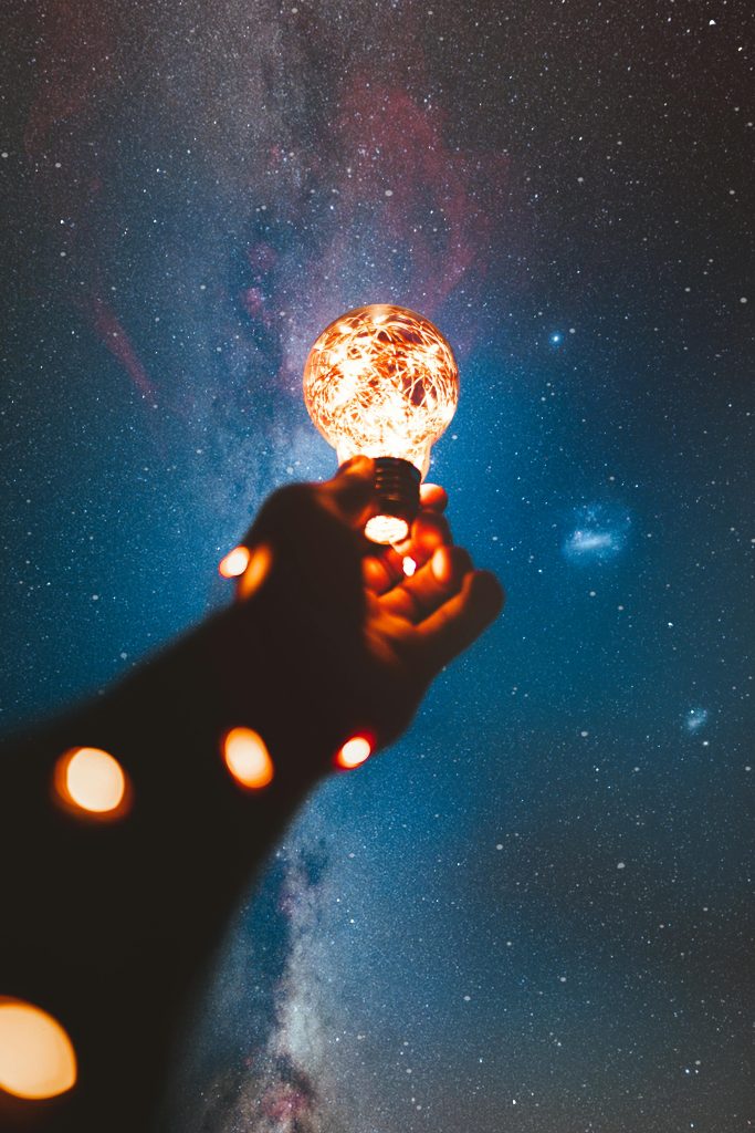 Oustretched arm holding a light bulb in frront of a starry background