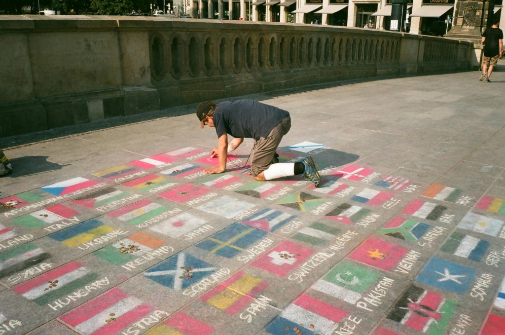 man on knees drawing many countries' flags with chalk