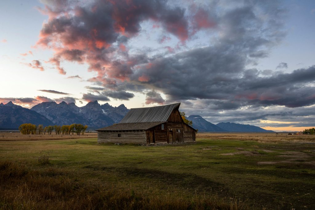 Old barn set back on a prairie with pink and gray clouds in the background.